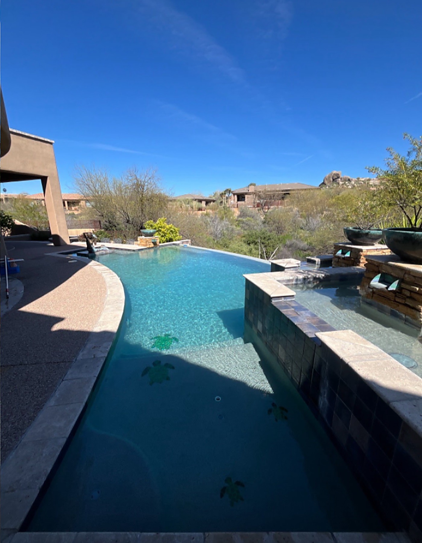 After: the same infinity-edge pool filled with sparkling turquoise water over restored plaster and turtle mosaic tile